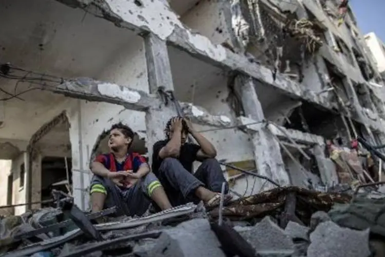 Irmãos palestinos observam os escombros de sua casa, em frente a um prédio de apartamentos, na Faixa de Gaza (Marco Longari/AFP)