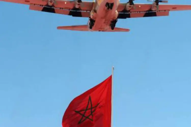 Um avião militar Hércules C-130, mesmo modelo do envolvido no acidente, voa por sobre uma bandeira do Marrocos
 (Aida/AFP)