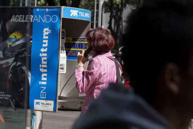 Mulher usa um telefone público da Telmex, uma subsidiária da América Móvil, na Cidade do México (Susana Gonzalez/Bloomberg)
