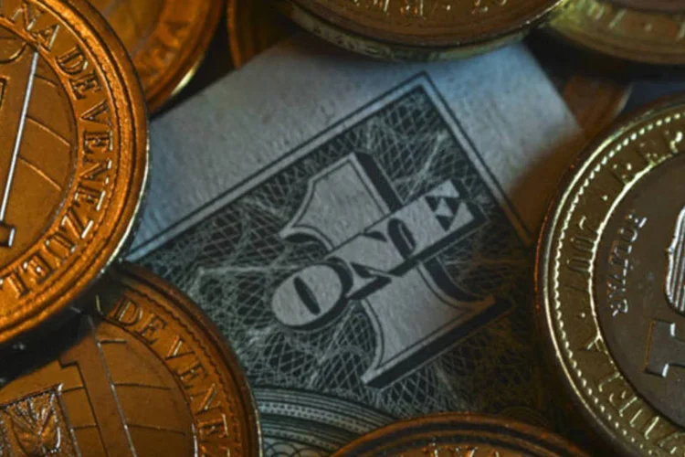 
	Medas de Bol&iacute;var e uma nota de um D&oacute;lar em Caracas, na Venezuela:&nbsp;bol&iacute;var foi negociado a uma cota&ccedil;&atilde;o 80% mais fraca quando comparada &agrave; taxa oficial de c&acirc;mbio
 (Meridith Kohut/Bloomberg)