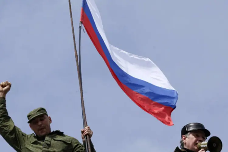 
	Homem segura bandeira russa em base naval ucraniana: &nbsp;mil&iacute;cia, denunciada pelo governo pr&oacute;-ocidental de Kiev como uma quadrilha a soldo de Moscou, acompanha as for&ccedil;as da R&uacute;ssia na tomada de instala&ccedil;&otilde;es
 (Vasily Fedosenko/Reuters)