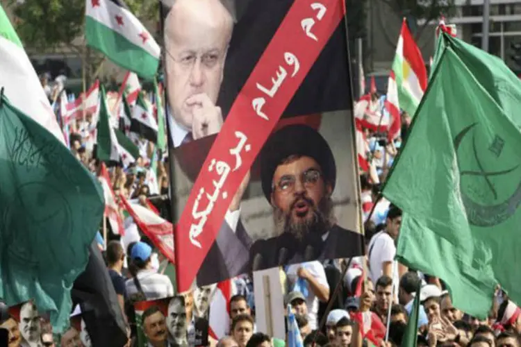 Milhares de pessoas carregam bandeiras, incluindo da oposição síria, e um cartaz com as imagens do líder do Hezbollah, Sayyed Hassan Nasrallah  (REUTERS World)