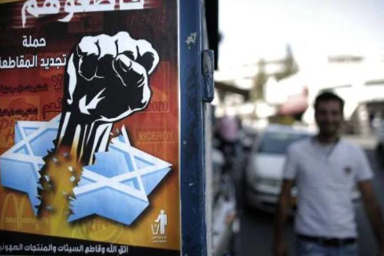 Um palestino caminha perto de um cartaz que convida ao boicote a produtos israelenses, em Jerusalém, devido aos sucessivos ataques na Faixa da Gaza (Ahmad Gharabli/AFP)