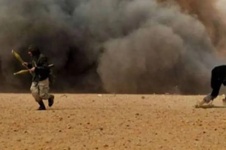 Rebeldes fogem de explosões durante um combate nos arredores da cidade de Ras Lanuf (Roberto Schmidt/AFP)