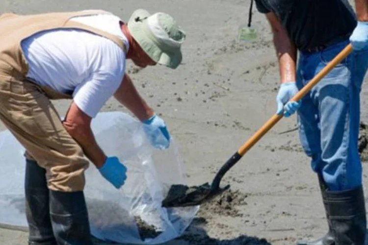 Trabalhadores limpam areia suja em praia da Louisiana, nos EUA (Saul Loeb/AFP)