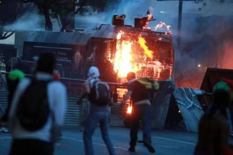 Manifestantes atacam veículos das forças de segurança durante protestos na Venezuela no domingo, 20 de abril (AFP)