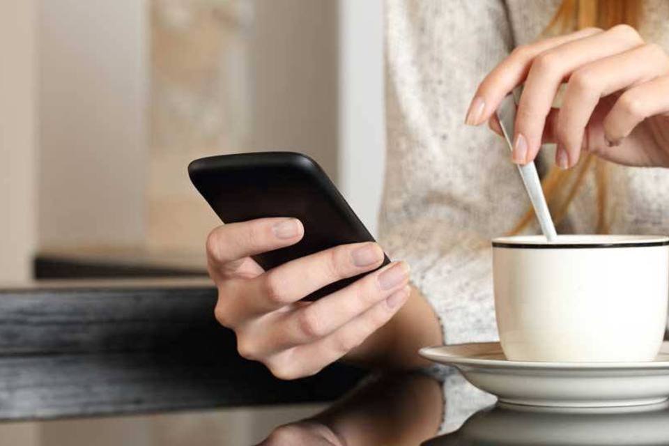 Mulher segura smartphone durante o café (AntonioGuillem/Thinkstock)
