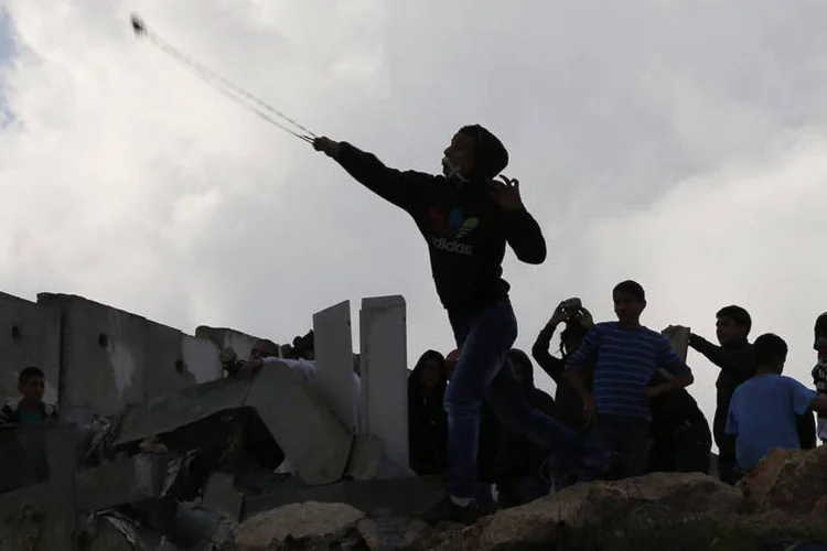 Refugiado palestino atira pedra contra israelense: residentes do campo de refugiados de Qalandia atiraram pedras contra soldados israelenses (Ammar Awad/Reuters)