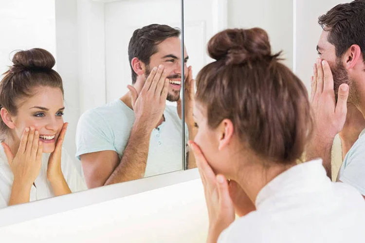Homem e mulher passam cosmético no rosto em frente ao espelho (4774344sean/Thinkstock)