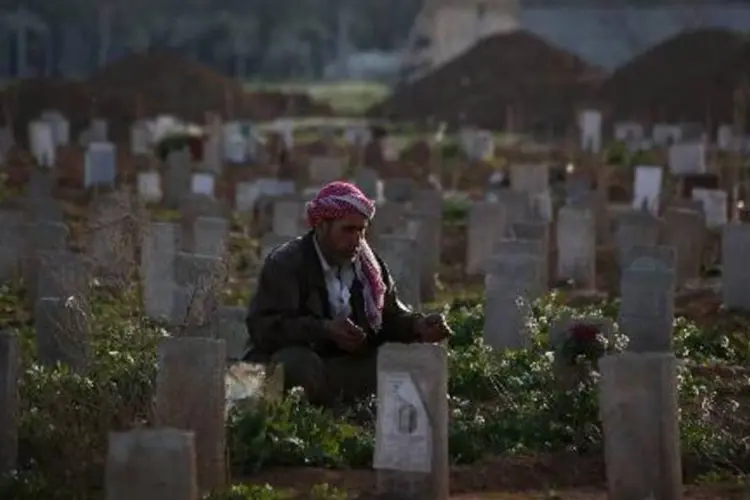 Homem reza diante do túmulo do filho, morto durante bombardeios, no cemitério do subúrbio de Duma, em Damasco (Abd Doumany/AFP)