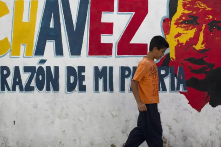 Menino passa por muro com imagem do presidente venezuelano, Hugo Chávez, em Caracas (REUTERS/Carlos Garcia Rawlins)