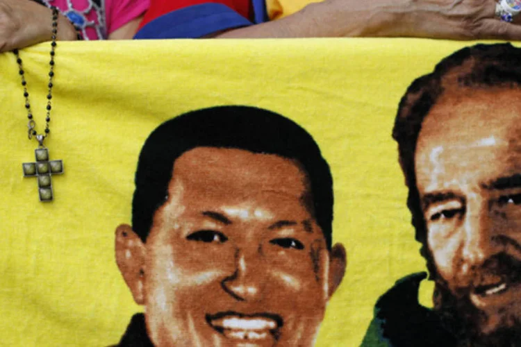 Apoiador do presidente venezuelano, Hugo Chávez, segura crucifixo perto da imagem de Chávez e do ex-líder Fidel Castro (D), em Caracas (Carlos Garcia Rawlins/Reuters)