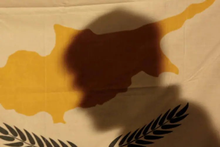 
	Sombra de manifestante em bandeira do Chipre: parceiros da ilha na zona do euro concordaram com um pacote de resgate de 10 bilh&otilde;es de euros na &uacute;ltima segunda-feira
 (REUTERS/Yorgos Karahalis)