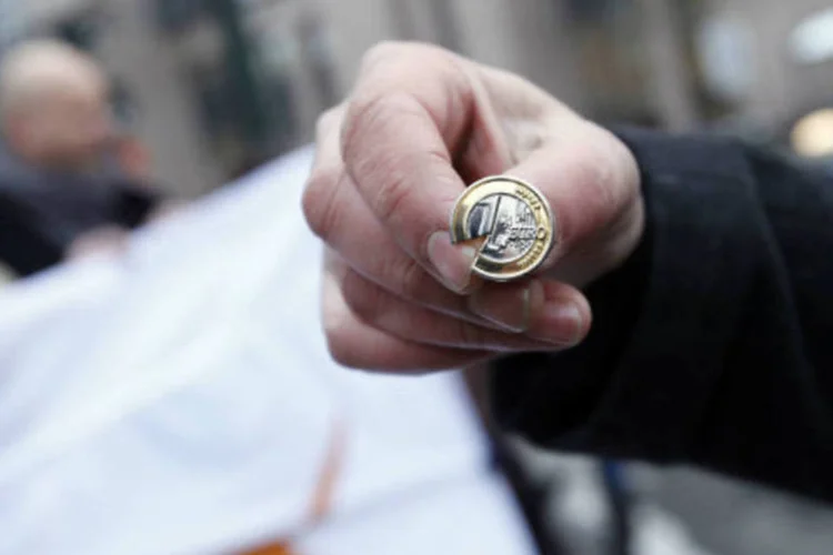 Homem segura moeda de 1 euro quebrada com bandeira do Chipre ao fundo, durante um protesto do lado de fora de uma reunião do Eurogrupo em Bruxelas (REUTERS / Sebastien Pirlet)