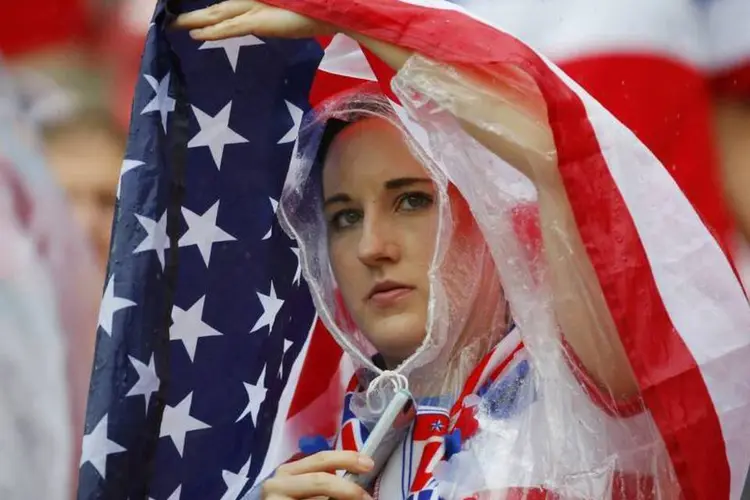Torcedora se protege da chuvas com uma bandeira dos EUA durante partida em Recife (Laszlo Balogh/Reuters)