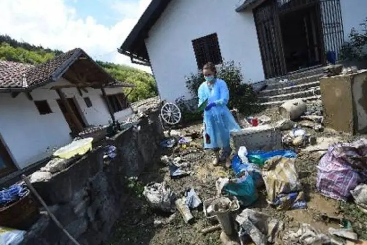 Protegida por equipamento médico, uma mulher recolhe seus pertences do lado de fora da casa alagada em Krupanj, 130 km ao sudoeste de Belgrado, em 20 de maio de 2014 (Andrej Isakovic/Reuters)