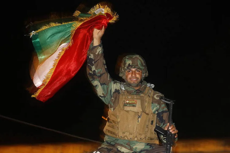 Combatente curdo peshmerga agita uma bandeira enquanto se move para a cidade síria de Kobani, na fronteira com a Turquia (Yannis Behrakis/Reuters)