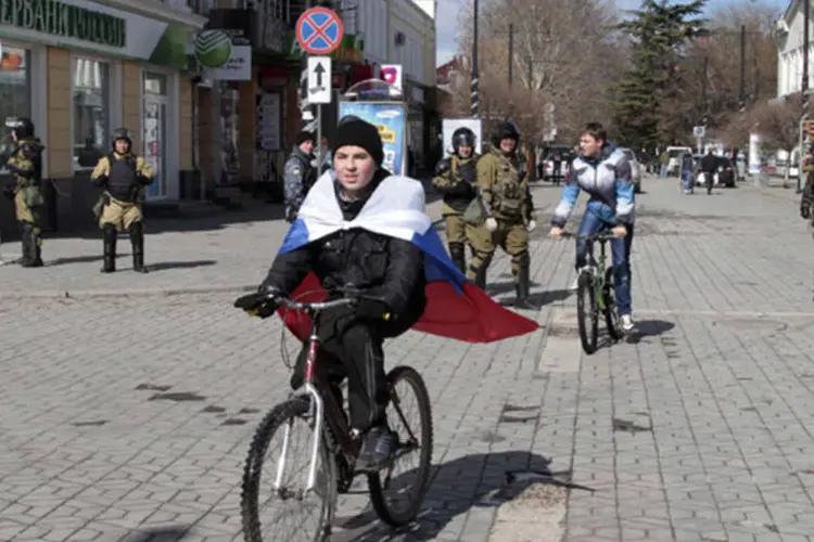 Um garoto envolto em uma bandeira da Rússia passa perto de membros de uma unidade de autodefesa da Crimeia, numa rua em Simferopol (Reuters)