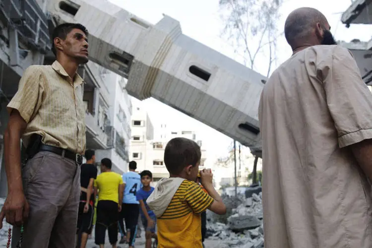 Palestinos ao lado dos destroços de uma mesquita após ataque aéreo de Israel, em Gaza (Finbarr OReilly/Reuters)