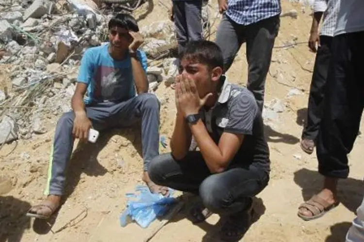 Palestinos choram ao verem o resgate do corpo de uma criança dos escombros de uma casa após um ataque aéreo israelense no sul da Faixa de Gaza (Said Jatib/AFP)