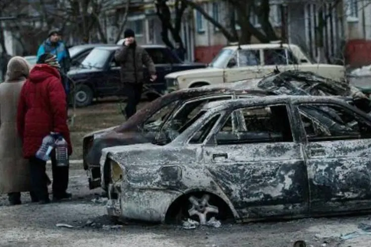 Pessoas olham para carros queimados em uma rua na cidade ucraniana de Mariupol, após ataque de rebeldes ucranianos que deixou 30 mortos (Anatolii Boiko/AFP)