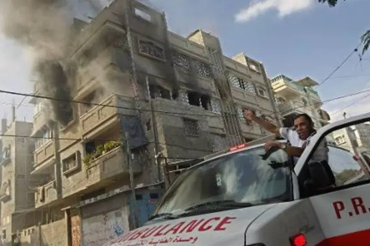 Membro da Cruz Vermelha e do Crescente Vermelho aponta para a fumaça que sai de um prédio depois de um ataque israelense no sul da faixa de Gaza (Said Khatib/AFP)
