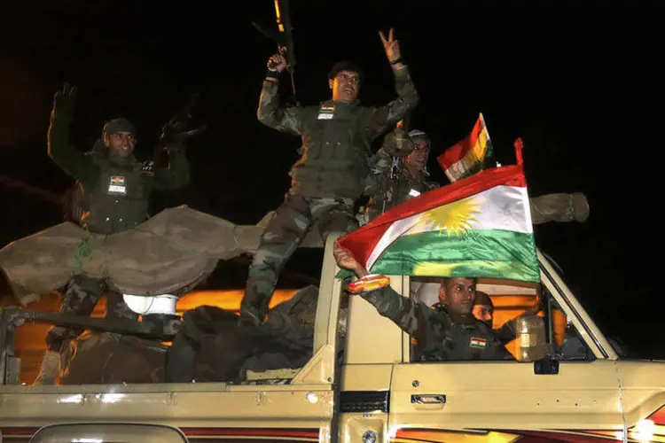 Combatentes curdos peshmerga agitam uma bandeira enquanto se movem para a cidade síria de Kobani, na fronteira com a Turquia (Yannis Behrakis/Reuters)