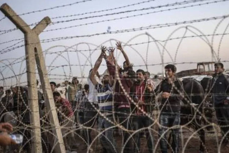 Curdos tentam pegar garrafas d'água lançadas por homem no lado turco da fronteira (Bulent Kilic/AFP)
