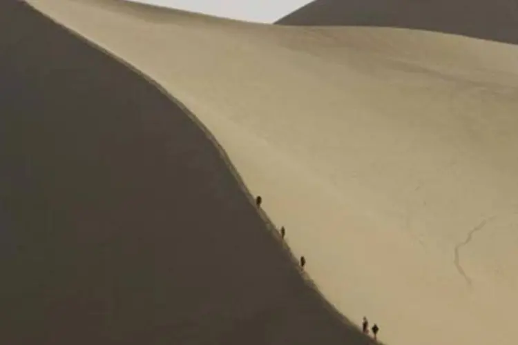 Turistas sobem de camelo uma duna do deserto que ameaça a cidade de Dunhuang, na China (Peter Parks/AFP)