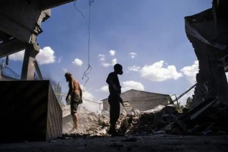 Homens retiram destroços após ataques aéreos à cidade de Donetsk, na Ucrânia (Dimitar Dilkoff/AFP)