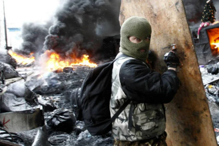 Homem se protege em meio a distúrbios em Kiev, na Ucrânia: centro de Kiev está envolto em fumaça no meio de ônibus carbonizados e carros destroçados (David Mdzinarishvili/Reuters)