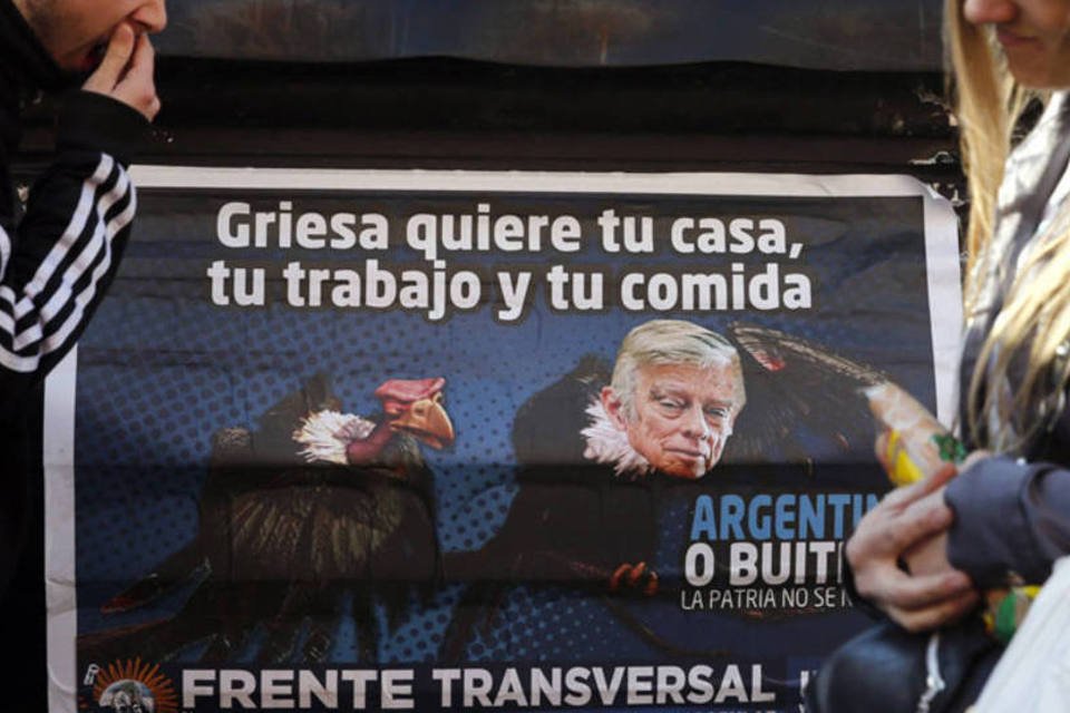 
	Pessoas passam por um poster que mostra o juiz americano Thomas Griesa como um abutre
 (Marcos Brindicci/Reuters)