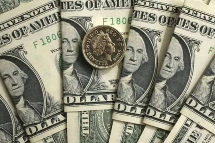 Dólares em notas embaixo de uma moeda de libra (Christopher Furlong/Getty Images)