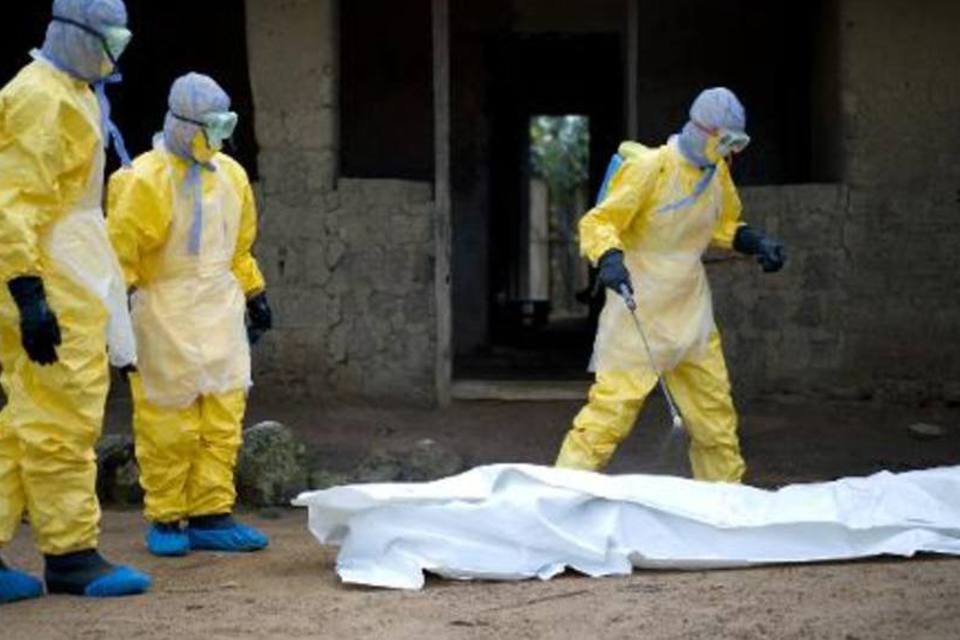 
	Equipes de s&aacute;ude da Cruz Vermelha ao redor de corpo de v&iacute;tima do Ebola na Guin&eacute;: no pa&iacute;s, multid&otilde;es atacaram centros de sa&uacute;de
 (Kenzo Tribouillard/AFP)