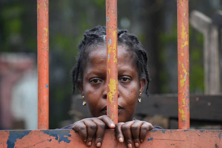 
	Uma moradora da favela West Point, na Lib&eacute;ria, olha por tr&aacute;s de port&atilde;o fechado
 (John Moore/Getty Images)