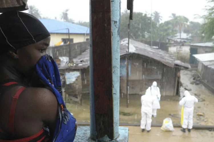 
	Mulher e trabalhadores usando roupa de prote&ccedil;&atilde;o contra o ebola, em Monr&oacute;via, Lib&eacute;ria
 (2Tango/Reuters)