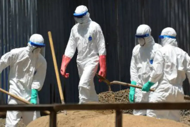 Trabalhadores sanitários usam trajes protetores enquanto depositam areia para absorver fluidos emitidos pelos corpos de vítimas do ebola (Zoom Dosso/AFP)
