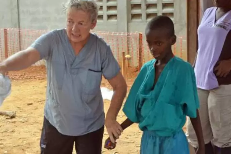 Um menino de 10 anos que perdeu a mãe, infectada pelo vírus Ebola, caminha com uma missionária, após ser liberado da quarentena, na capital liberiana, Monróvia (Zoom Dosso/AFP)