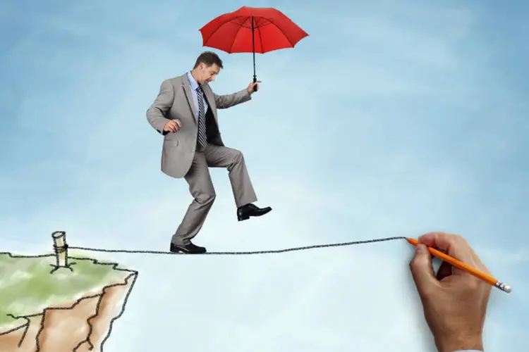 Executivo/empreendedor se equilibrando em corda bamba com guarda-chuva (desafios) (BrianAJackson/Thinkstock)
