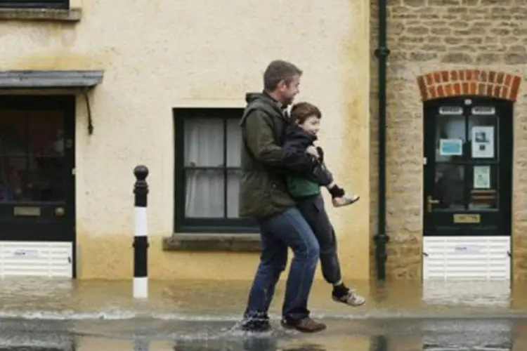 
	Homem e crian&ccedil;a atravessam enchente no Reino Unido: outras 70.000 resid&ecirc;ncias est&atilde;o amea&ccedil;adas pelas inunda&ccedil;&otilde;es no pa&iacute;s
 (Justin Tallis/AFP)