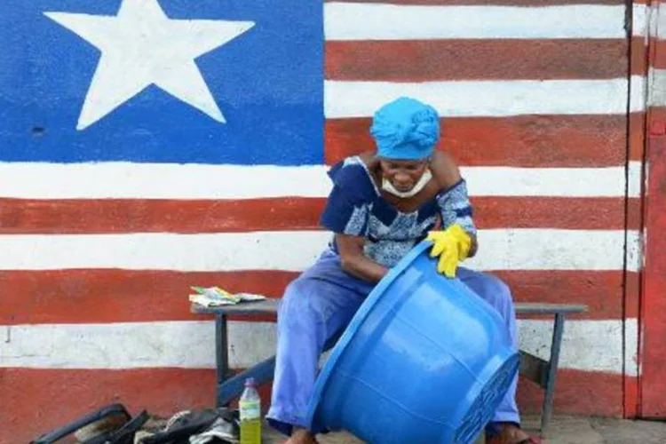 Mulher sentada em mural com a bandeira da Libéria limpa bacia: país segue como um dos mais afetado pela epidemia de ebola (Dominique Faget/AFP)