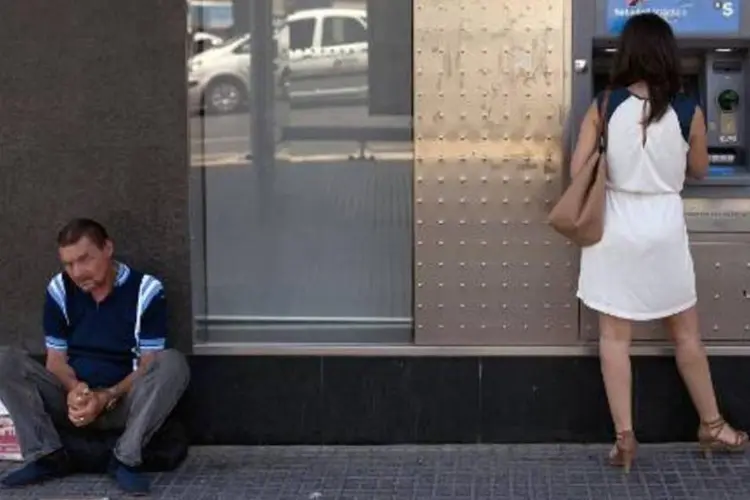 Homem pede esmolas enquanto uma mulher saca dinheiro na Espanha (Jorge Guerrero/AFP)