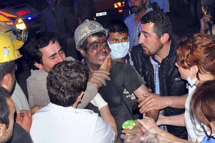 Mineiro é cercado após ser resgatado de uma mina de carvão, onde ocorreu uma explosão, em Soma, na Turquia (Ihlas/Yilmaz Saripinar/Reuters)