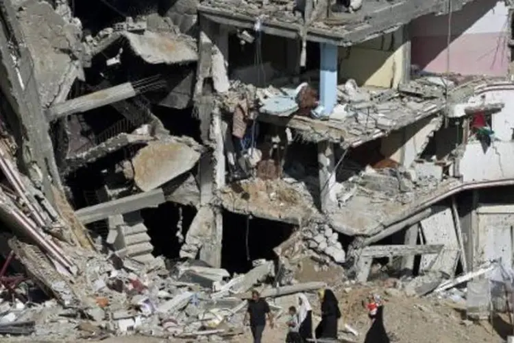 Família palestina caminha diante de edifício destruído no conflito entre o Hamas e o exército israelense em Shejaiya (Roberto Schmidt/AFP)