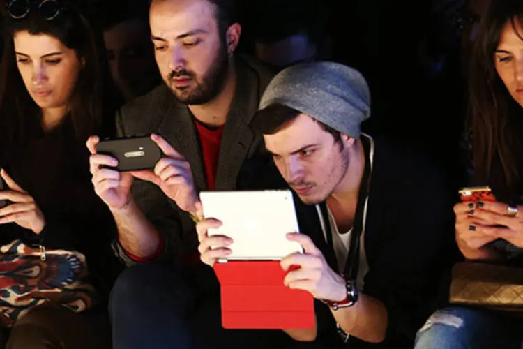 
	Jovens olham para tela de smartphones e tablets: feita &eacute; totalmente virtual
 (Andreas Rentz/Getty Images)