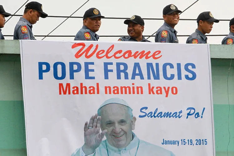 Membros da Polícia Nacional das Filipinas passam por cartaz com mensagem de boas-vindas ao papa Francisco (REUTERS/ Cheryl Ravelo)