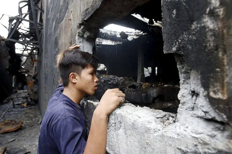 
	Sobrevivente olha pela janela de f&aacute;brica que pegou fogo nas Filipinas: os bombeiros levaram sete horas para controlar o fogo
 (REUTERS/Erik De Castro)