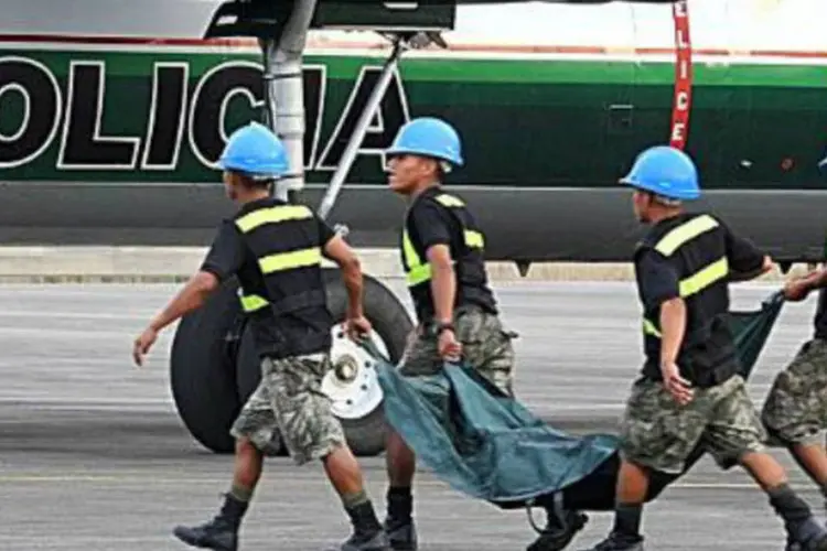 Policiais peruanos carregando corpo de terrorista morto: corpos de 26 crianças e 18 mulheres estavam em fossas comuns (AFP)