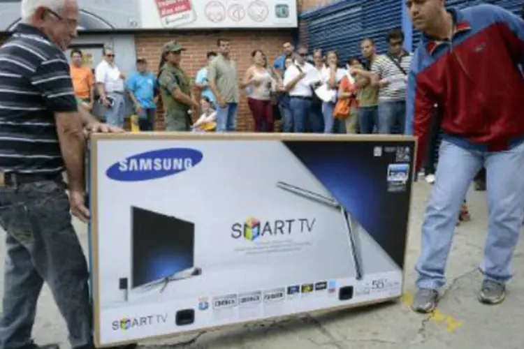 Homens carregam TV em loja obrigada pelo governo a baixar os preços na Venezuela: reduções de preços levaram milhares de venezuelanos às lojas (Leo Ramírez/AFP)