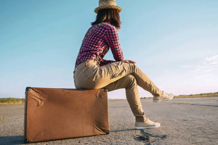 Garota sentada em cima da mala, simbolizando viagens (Remains/Thinkstock)